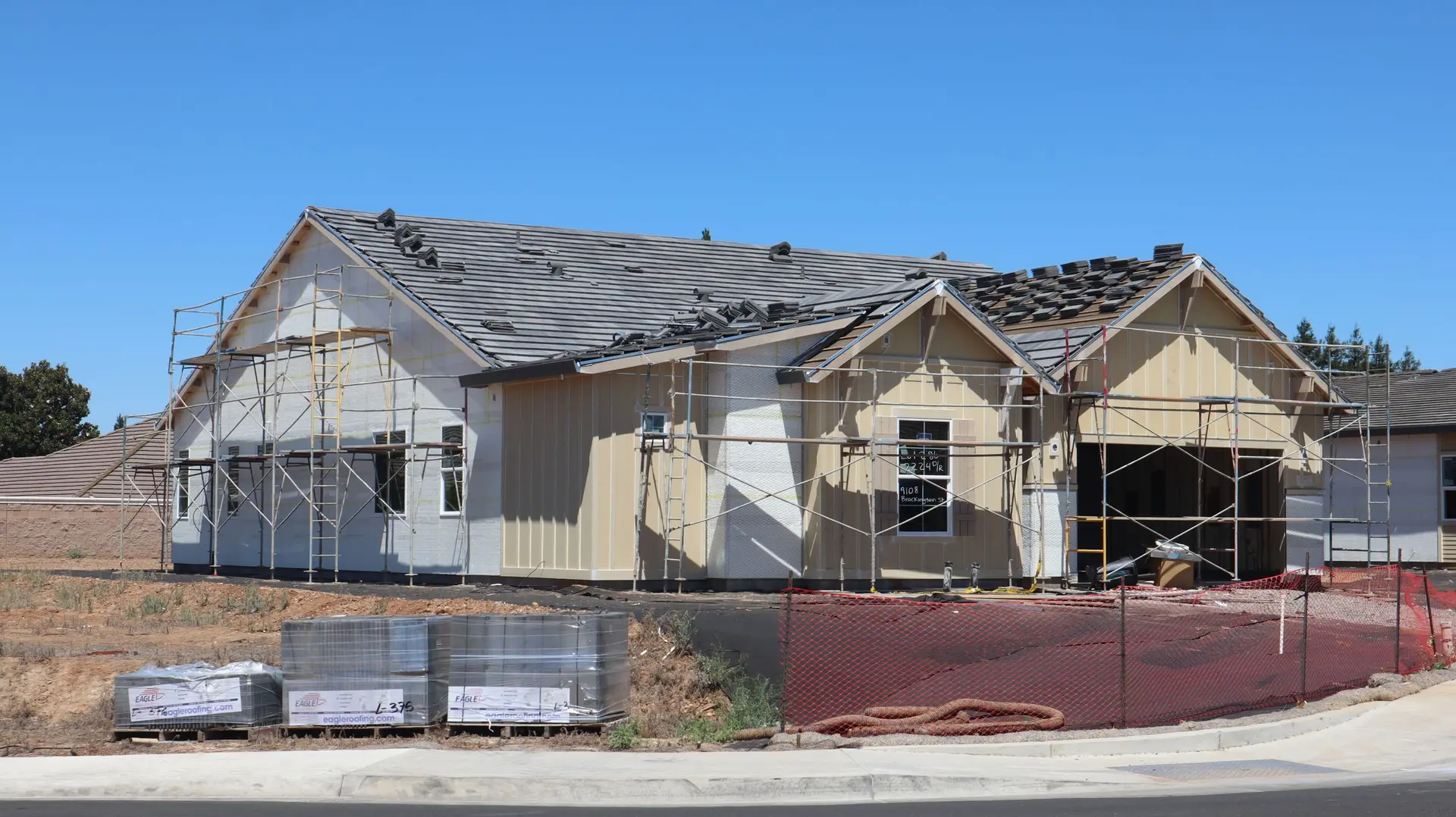 Single-story house under construction with scaffolding and roofing stacked out front