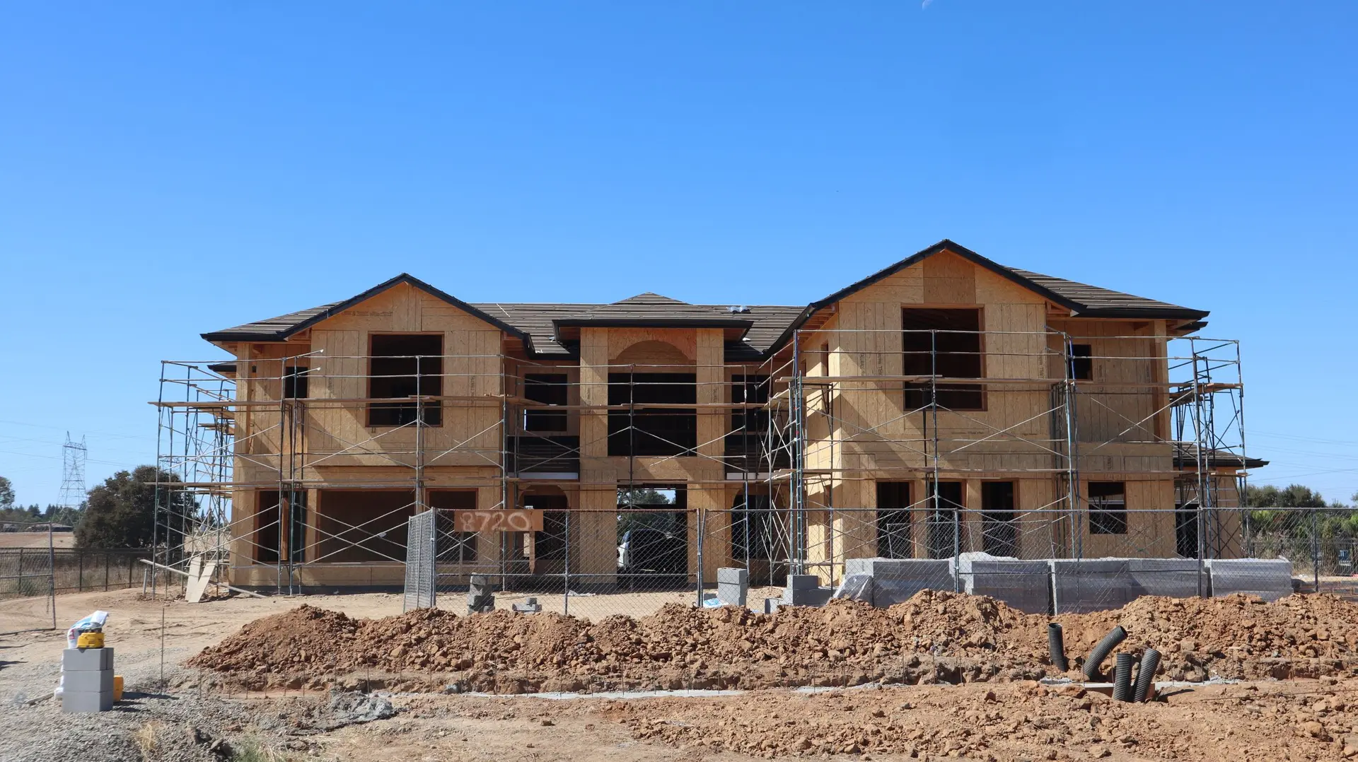 Two-story house framed and sheathed behind scaffolding on a dirt lot