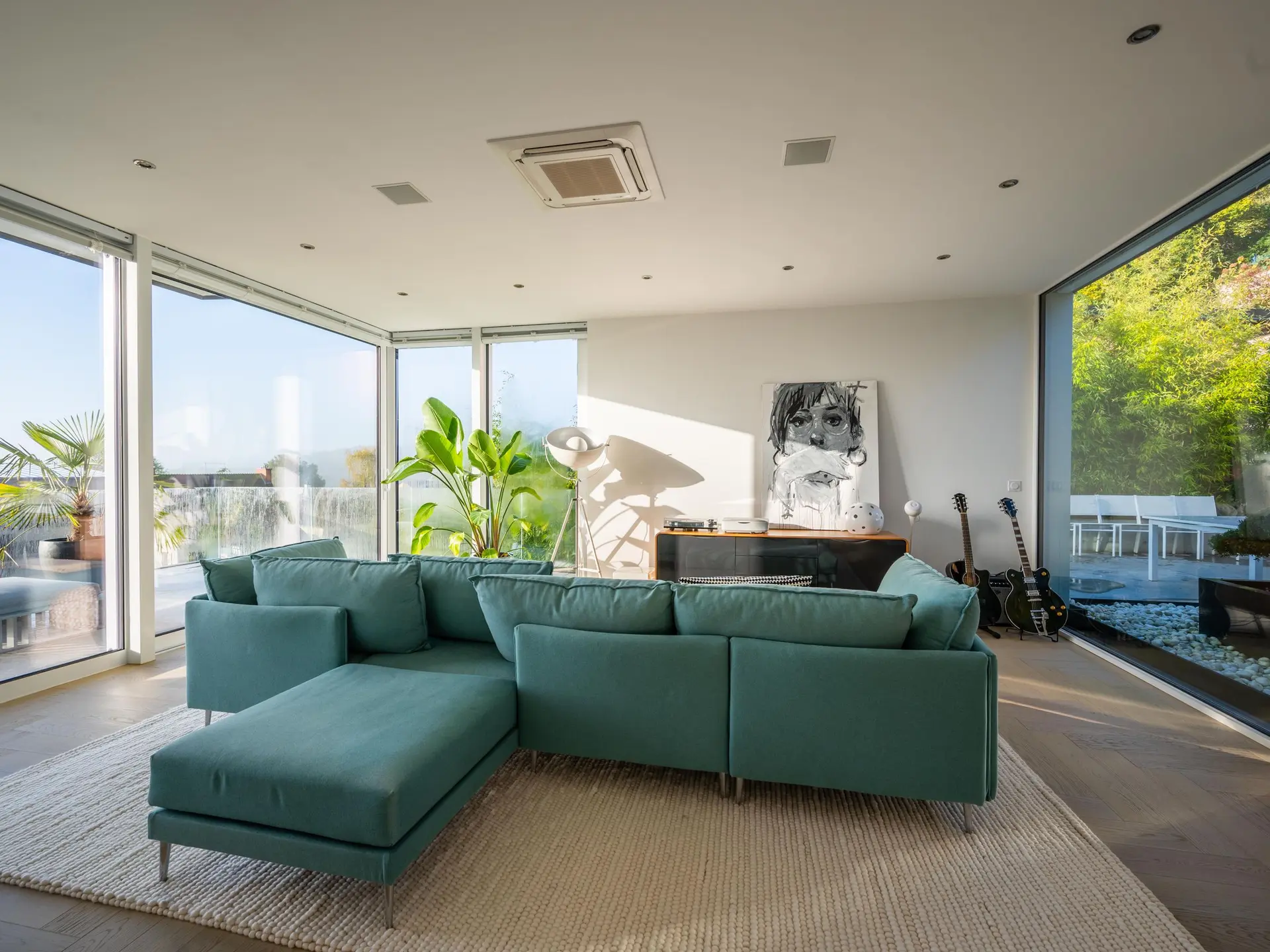 Living room with a teal sectional and corner windows onto greenery